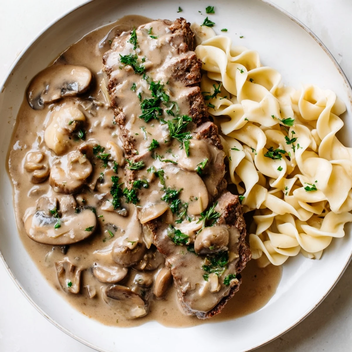 A hearty bowl of classic Beef Stroganoff with Mushroom Gravy over Noodles, garnished with fresh parsley on a rustic table.