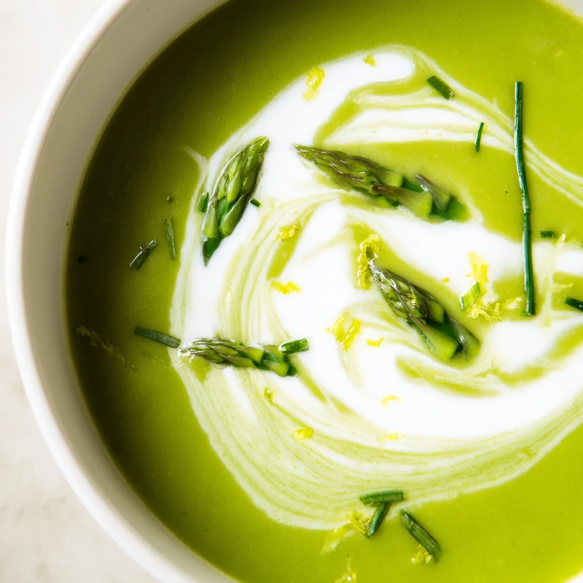 Creamy Asparagus Soup with Lemon and Crème Fraîche in a white bowl, garnished with fresh chives and lemon zest.