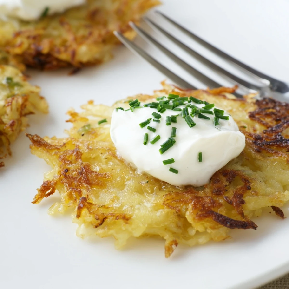 Golden brown Crispy Potato Latkes with sour cream and chives on a white plate.