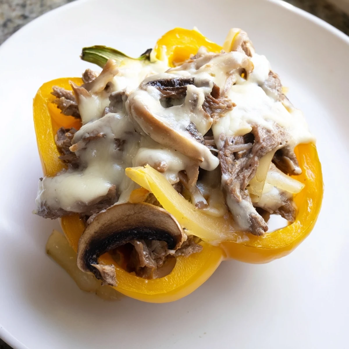 Four colorful roasted bell peppers overflowing with savory sautéed beef, onions, and melted cheese for a delicious low-carb meal.