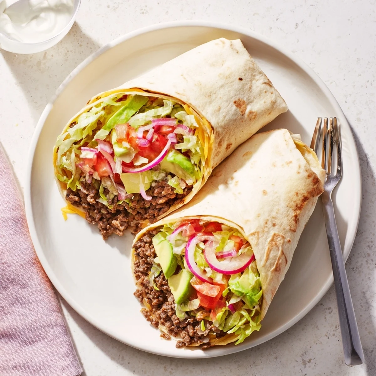The Beef Lunch Wrap Tortilla showcases golden, warm flour tortillas stuffed with seasoned ground beef, diced tomatoes, and a zesty lime sour cream sauce.  