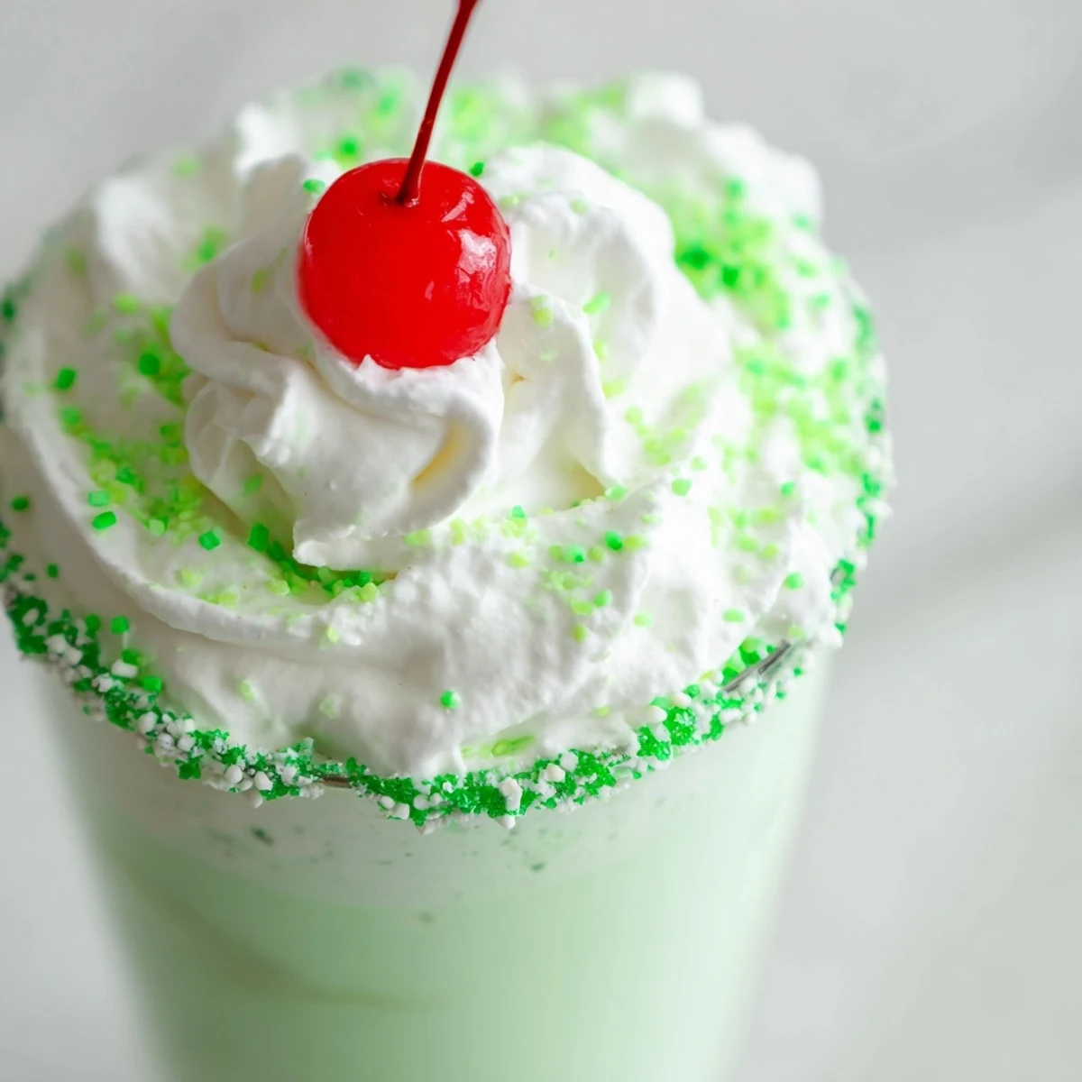 Two glasses of Shamrock Mint Milkshake topped with whipped cream and a maraschino cherry, served with green straws.
