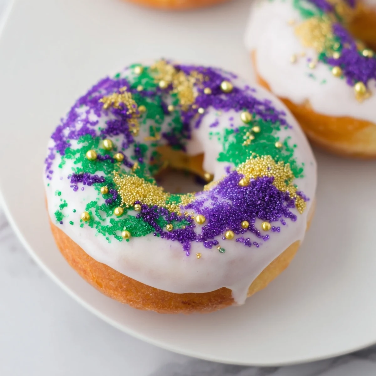 A close-up of a baked Mardi Gras King Cake Donut shows fluffy texture, creamy filling, and vibrant Mardi Gras-colored sugar.