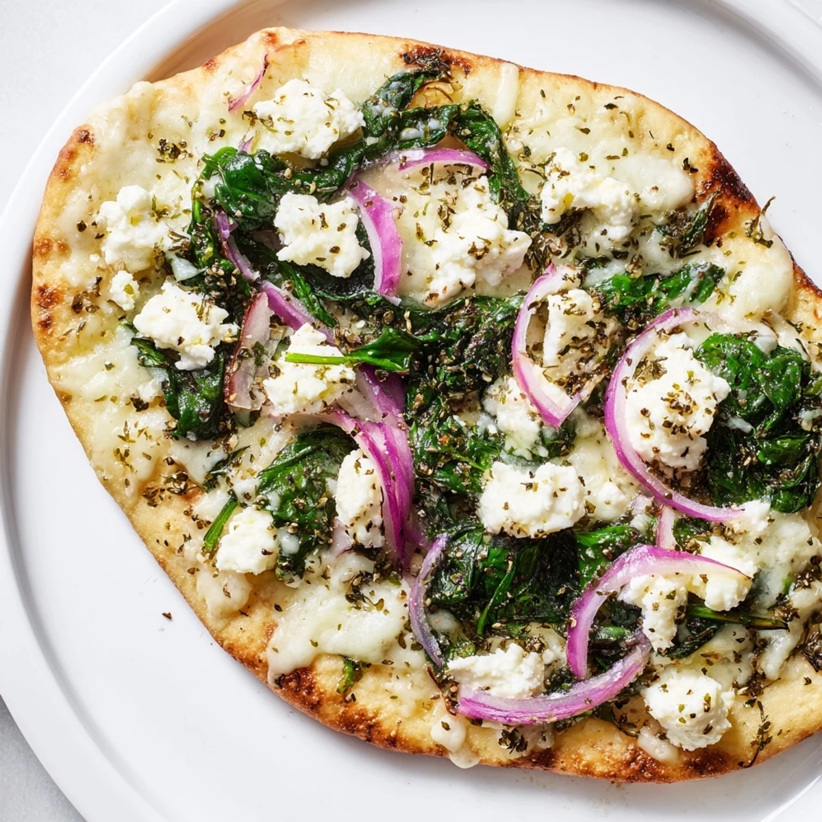 Golden-brown flatbread pizza topped with wilted spinach, creamy feta, and melted mozzarella on a baking sheet.  