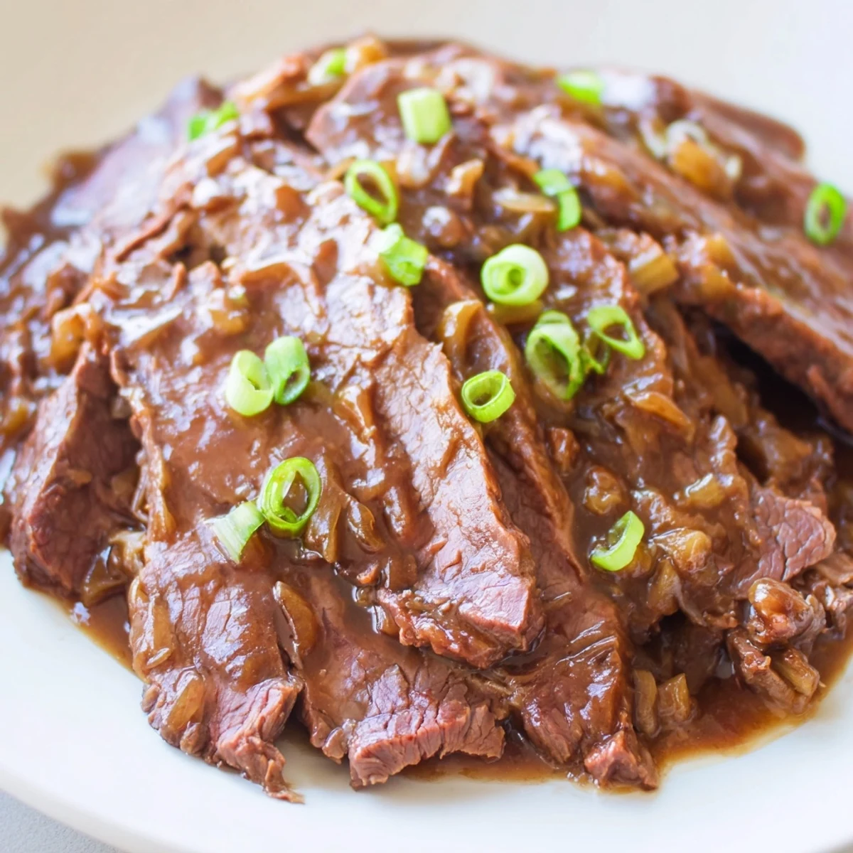 A slow cooker holds succulent Ultimate Slow Cooker Mongolian Beef garnished with green onions, paired with sautéed broccoli for a complete meal.