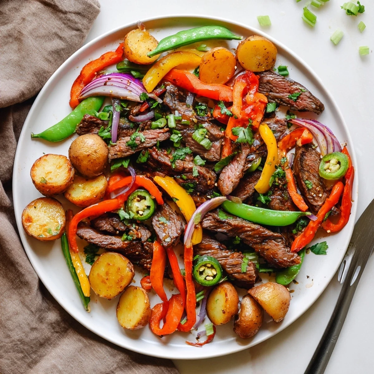 A close-up of Blackstone Cowboy Stir Fry Dinner sizzling on a griddle with seared beef, colorful peppers, and golden potatoes, garnished with fresh cilantro.