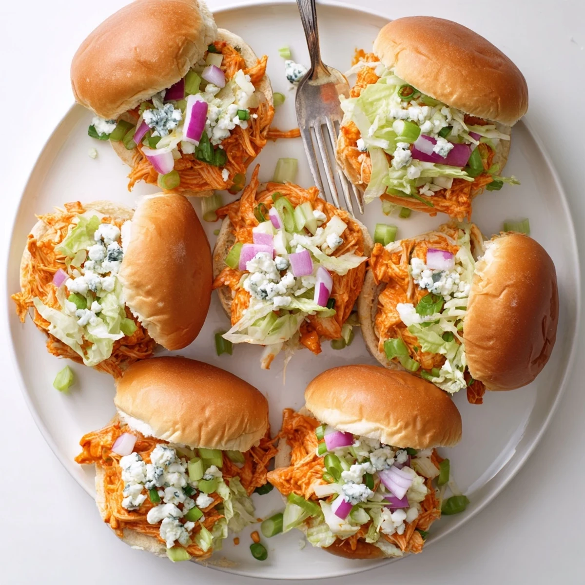 Close-up of warm spicy Buffalo chicken sliders on a bun, with melted blue cheese and fresh red onion.