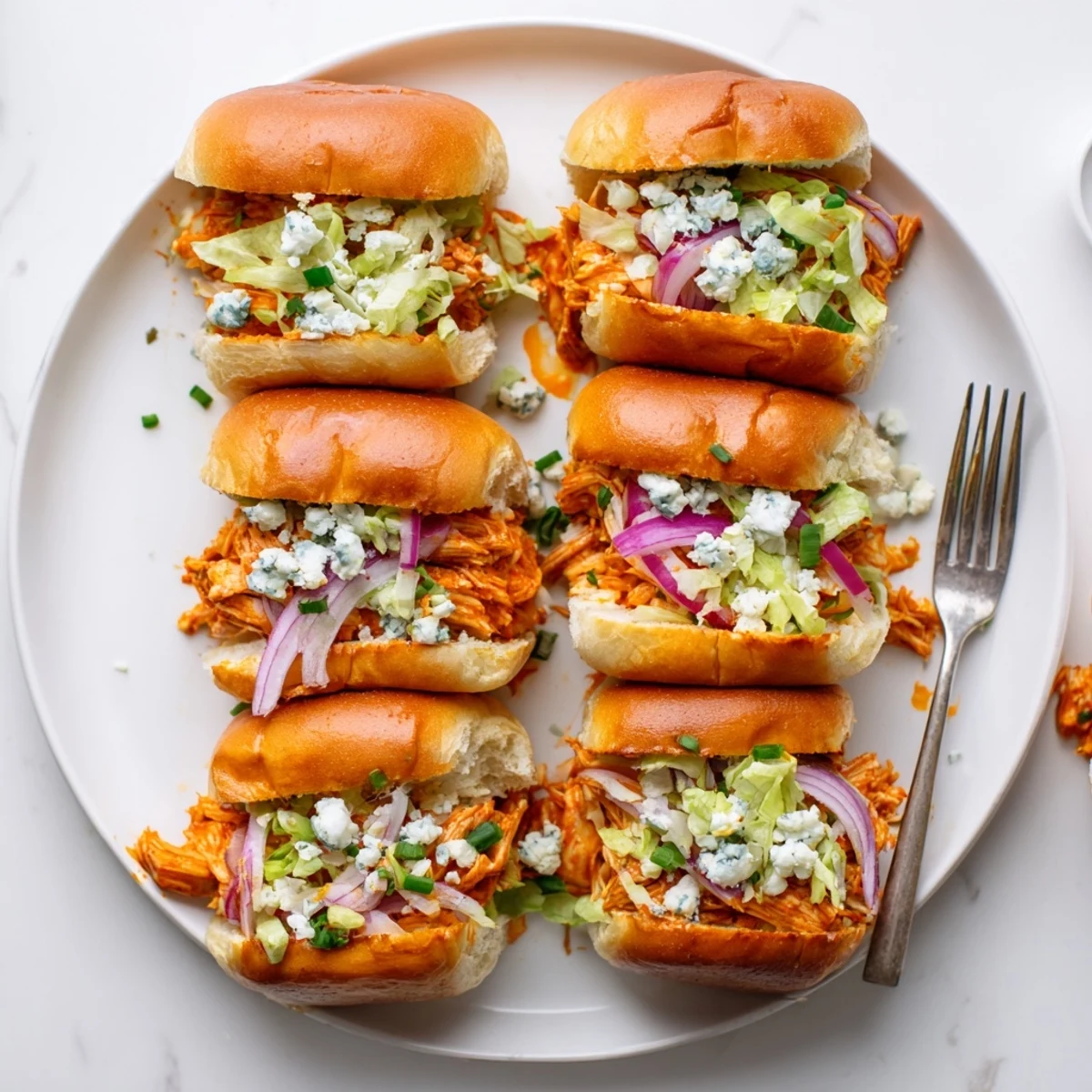 A platter of spicy Buffalo chicken sliders garnished with chives and served beside crunchy celery sticks.