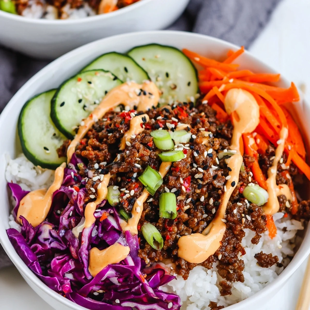 Golden sesame Korean beef bowl with fluffy rice, crunchy carrots, cucumbers, and a spicy mayo drizzle.