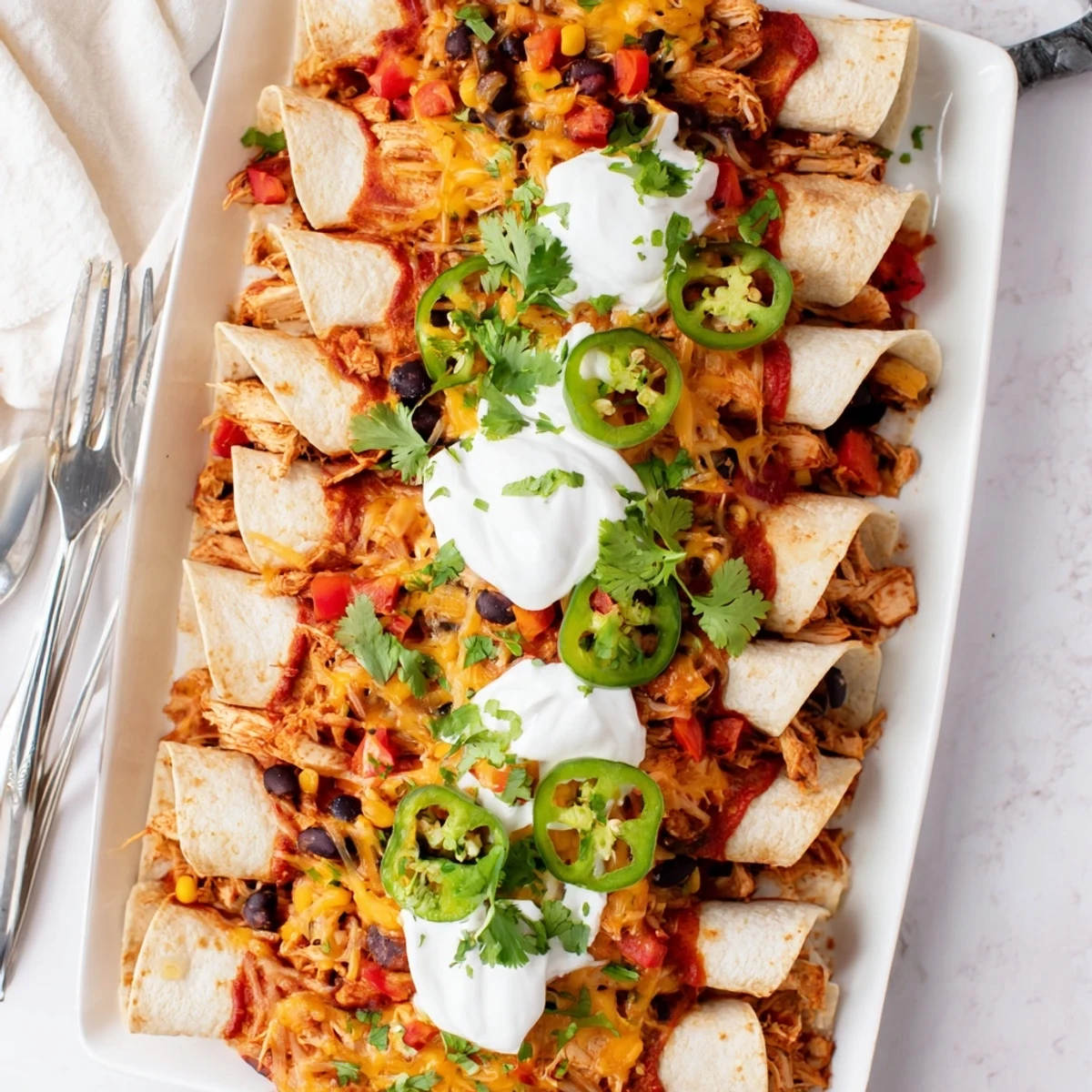 Golden-baked Chicken Enchiladas in a white dish, topped with melted cheese, fresh cilantro, and jalapeño slices.
