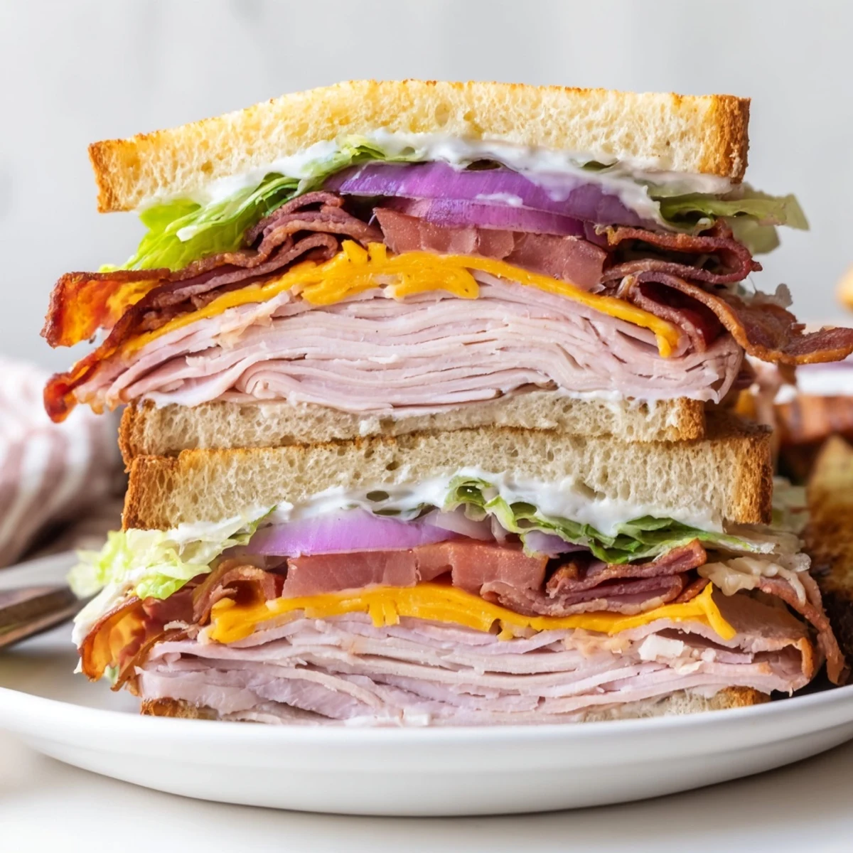 Hearty ultimate turkey beef bacon ranch sandwich cut in half revealing colorful layers of lettuce tomato and cheese