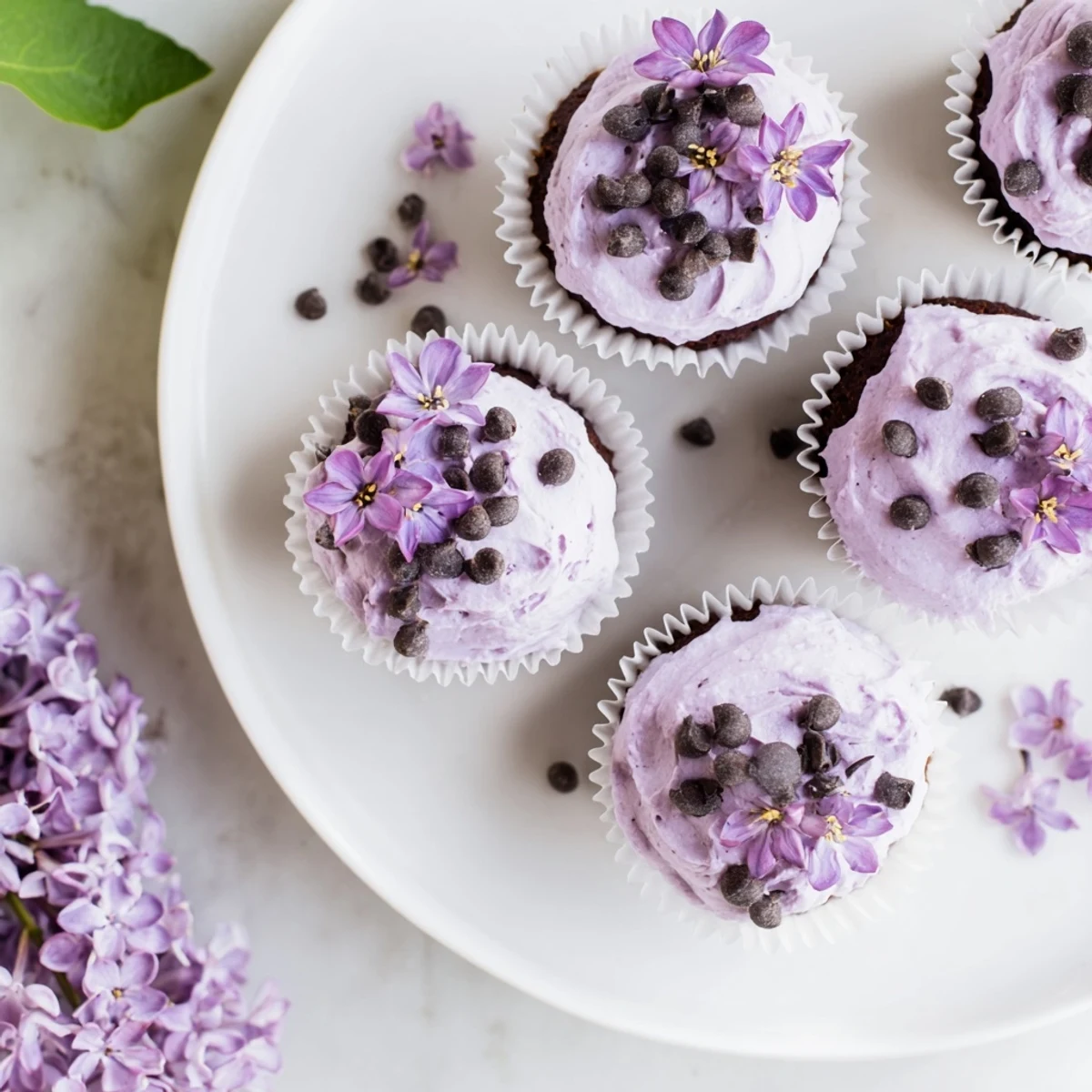 Moist chocolate lilac cupcakes with purple blossoms and lilac frosting on white plate