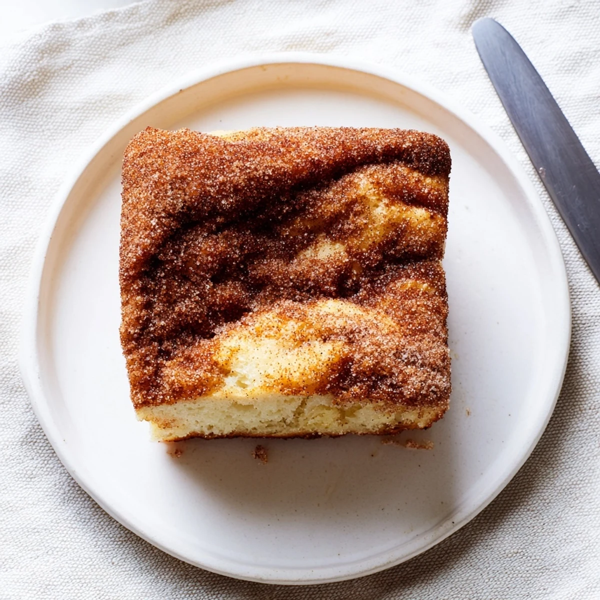 Warm slice of cinnamon sugar donut bread on a white plate topped with melted butter
