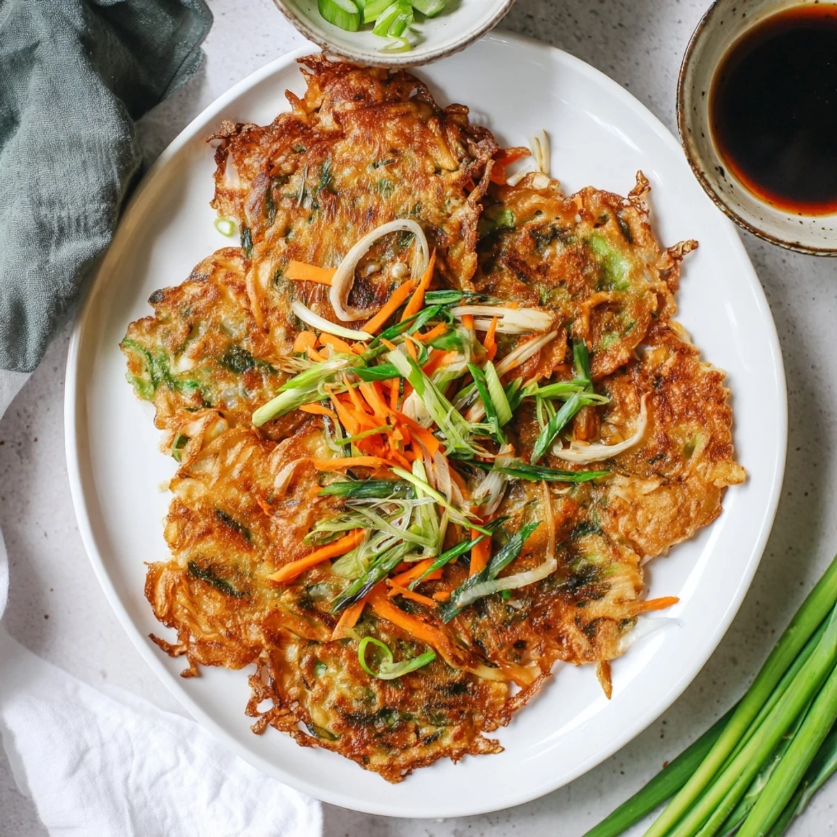Savory Korean pancakes served as wedges on a white plate alongside a small bowl of soy dipping sauce