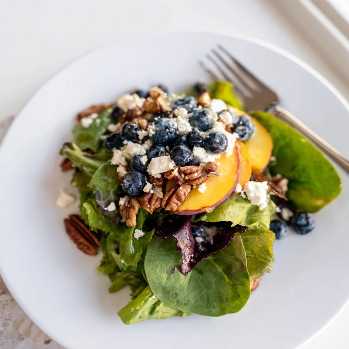 Colorful summer salad featuring juicy blueberries, sweet peaches, and creamy feta on crisp bed of greens