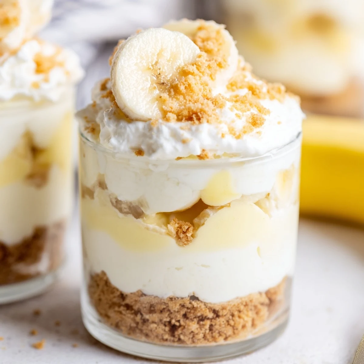Creamy no bake banana pudding cheesecake cups layered with fresh banana slices and vanilla wafer crumbs in individual glass jars