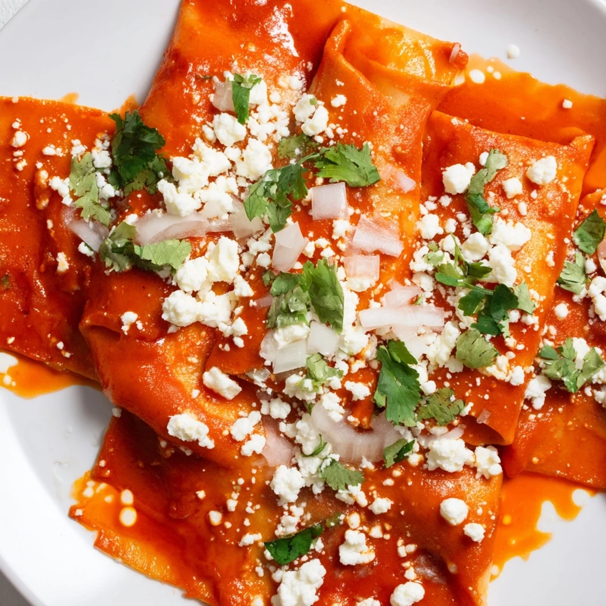 Entomatadas smothered in rich red tomato sauce with melted cheese and diced onion garnish