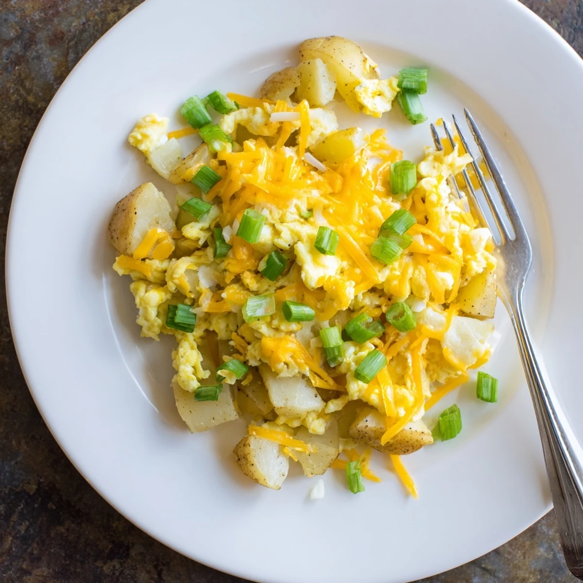 Golden cheesy potato egg scramble plated with soft eggs and melted cheddar cheese
