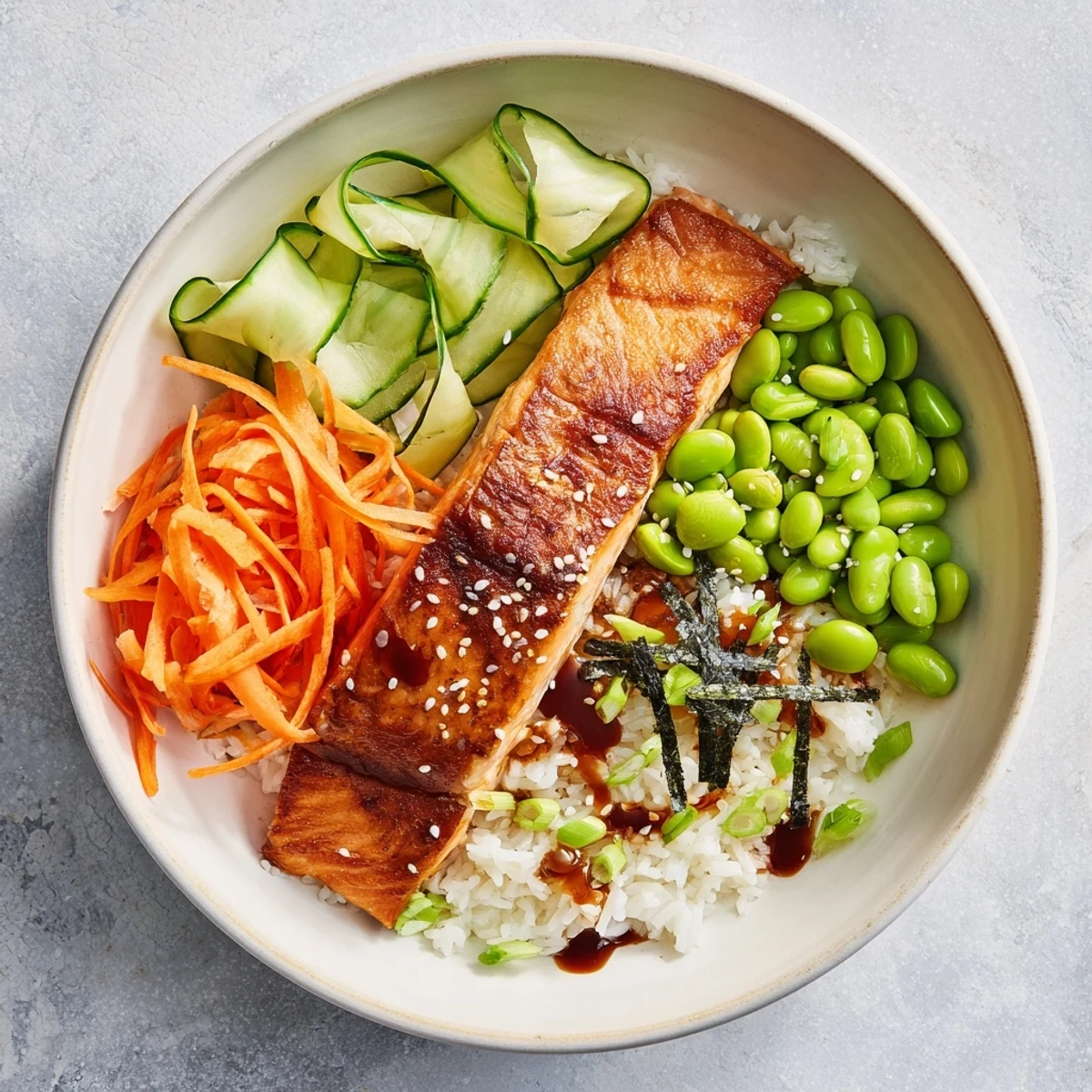 Skin-on crispy salmon pieces arranged atop steamed jasmine rice bowl with crisp vegetables, creamy avocado, and zesty sriracha honey sauce garnished with nori strips