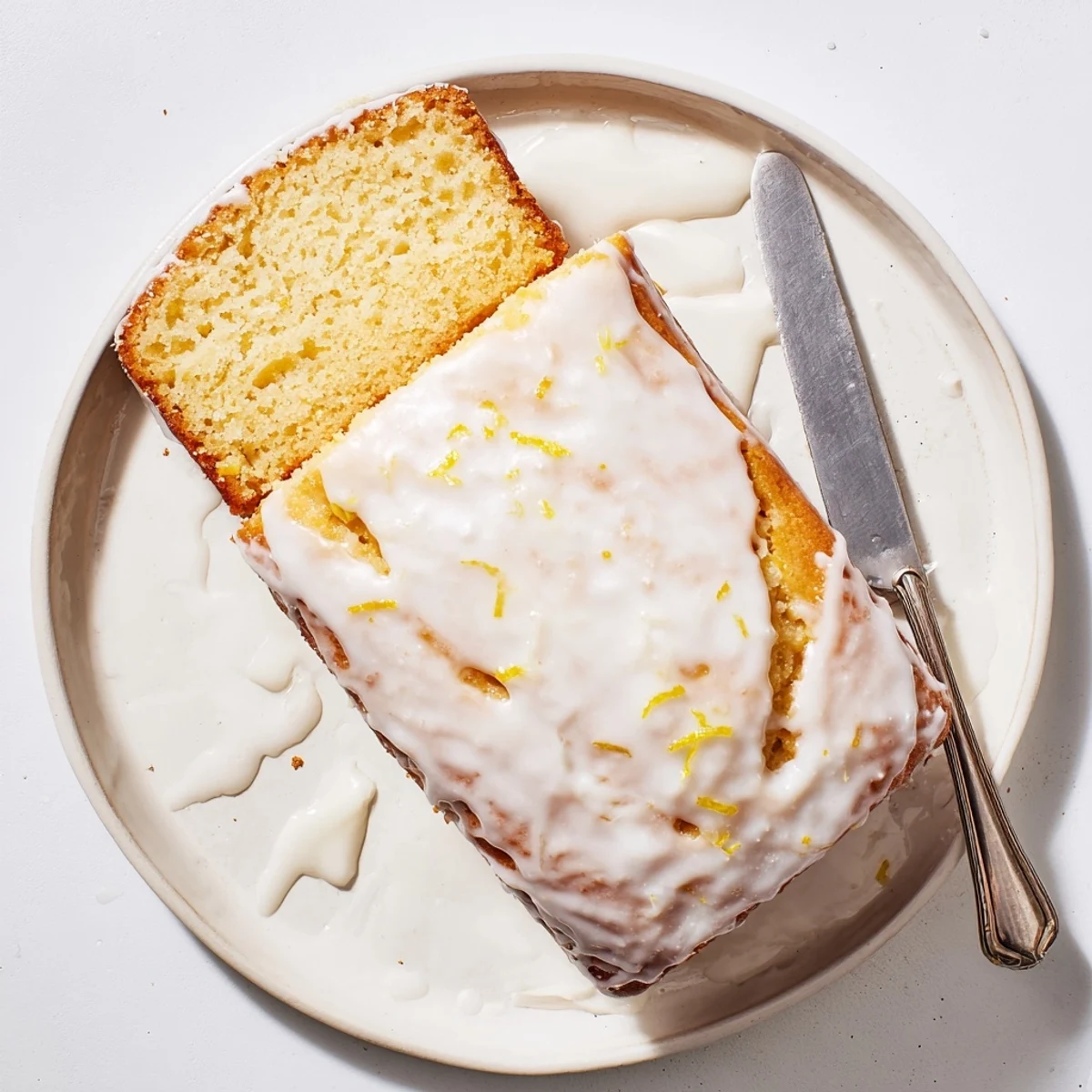 Golden Greek yogurt lemon loaf drizzled with white lemon glaze on a wooden cutting board