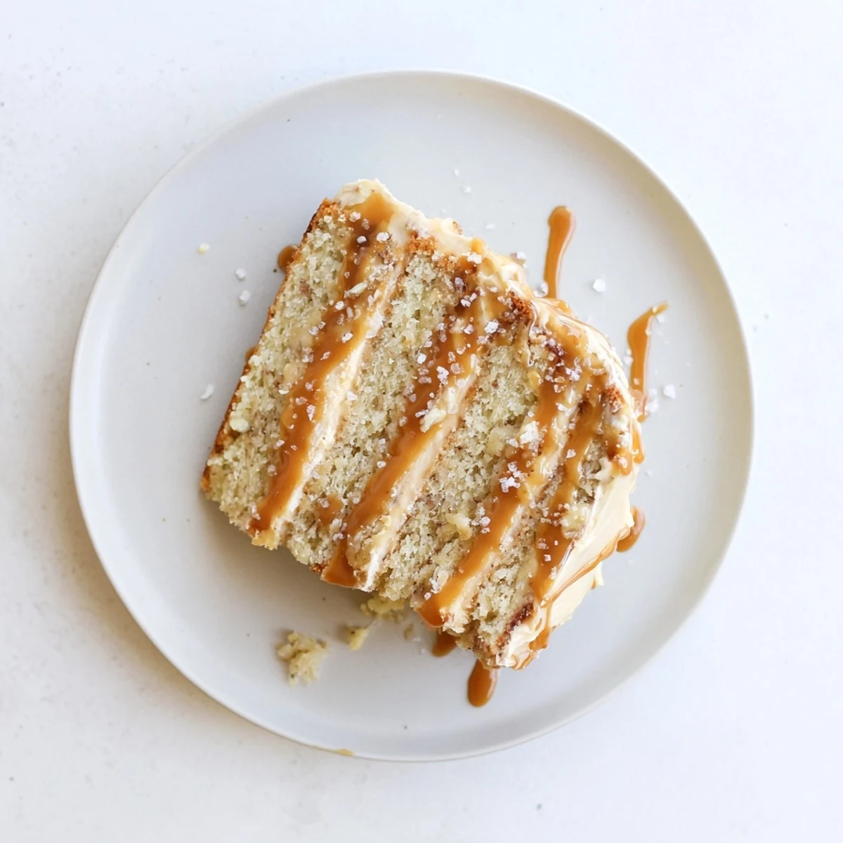 Decadent salted caramel brown butter banana cake with drippy caramel frosting and flaked sea salt garnish