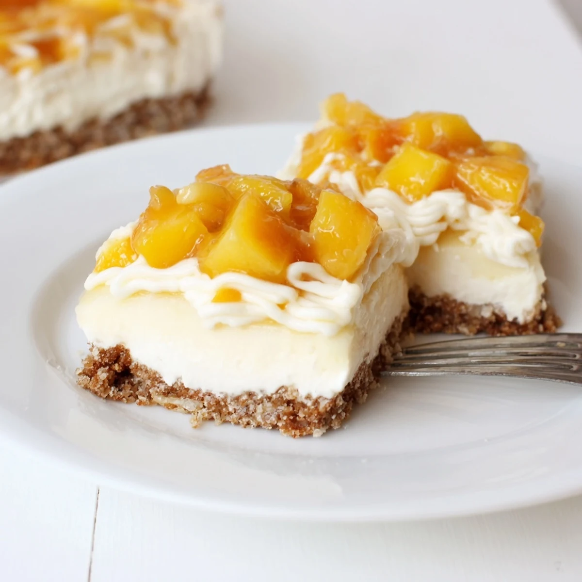 Creamy Peaches and Cream Cheesecake Bars topped with fresh peach slices and whipped cream drizzle