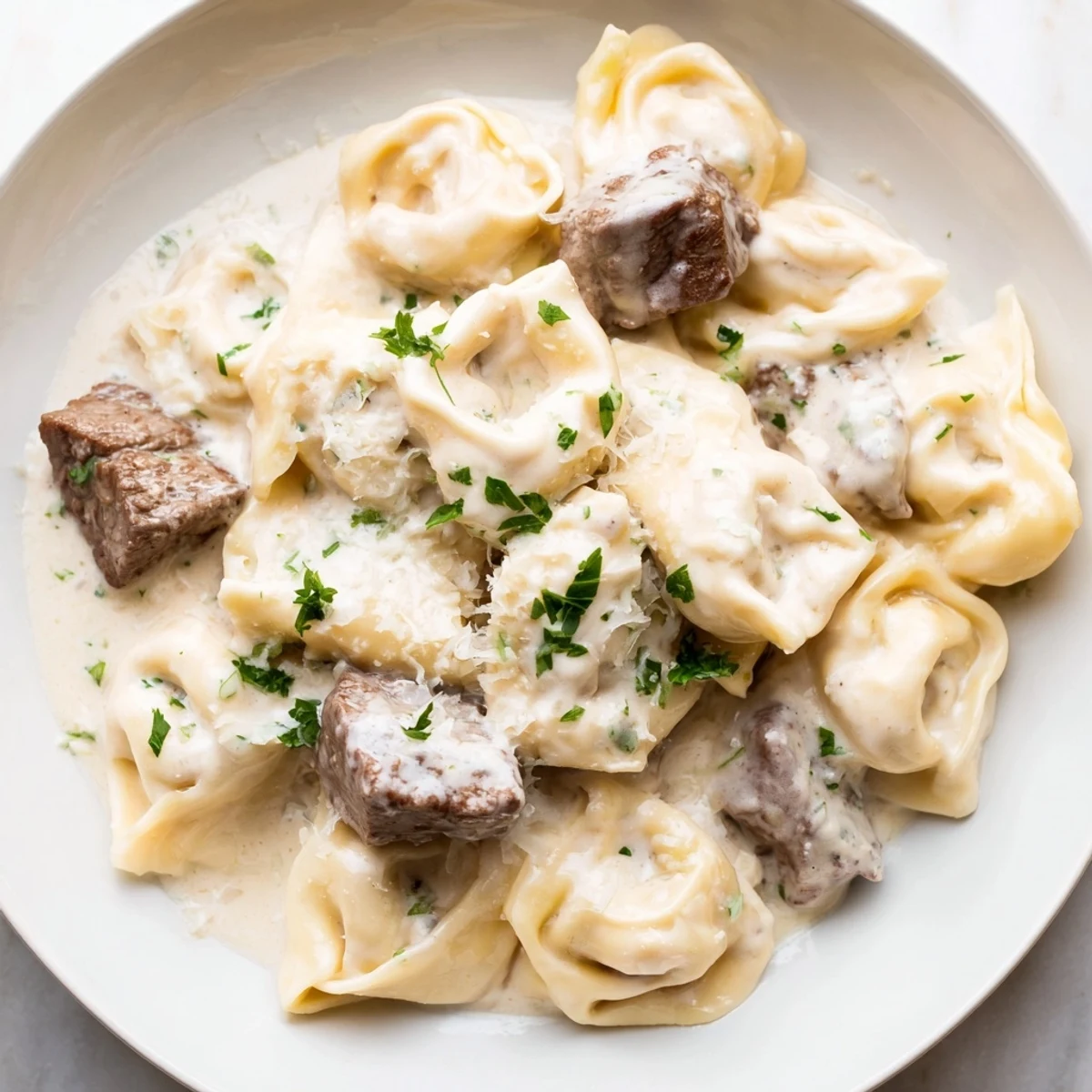 Garlic steak tortellini smothered in creamy Parmesan sauce with fresh parsley garnish