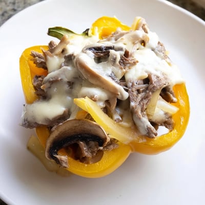 Four colorful roasted bell peppers overflowing with savory sautéed beef, onions, and melted cheese for a delicious low-carb meal.