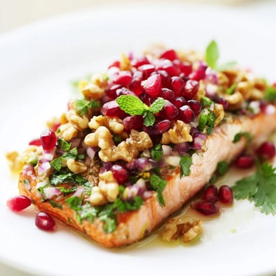 Perfectly flaky baked salmon topped with bright red pomegranate arils, chopped walnuts, and fresh mint leaves, ready to serve.